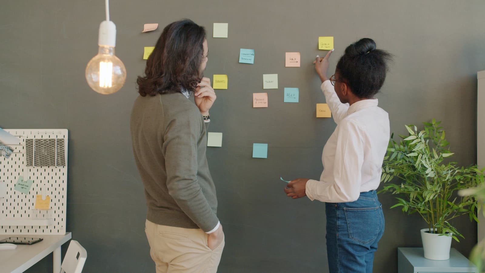 Twee collega's overleggen bij een glaswand vol gekleurde sticky notes tijdens een strategiesessie