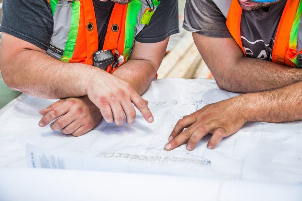 Bouwvakkers in veiligheidshesjes bespreken een bouwtekening