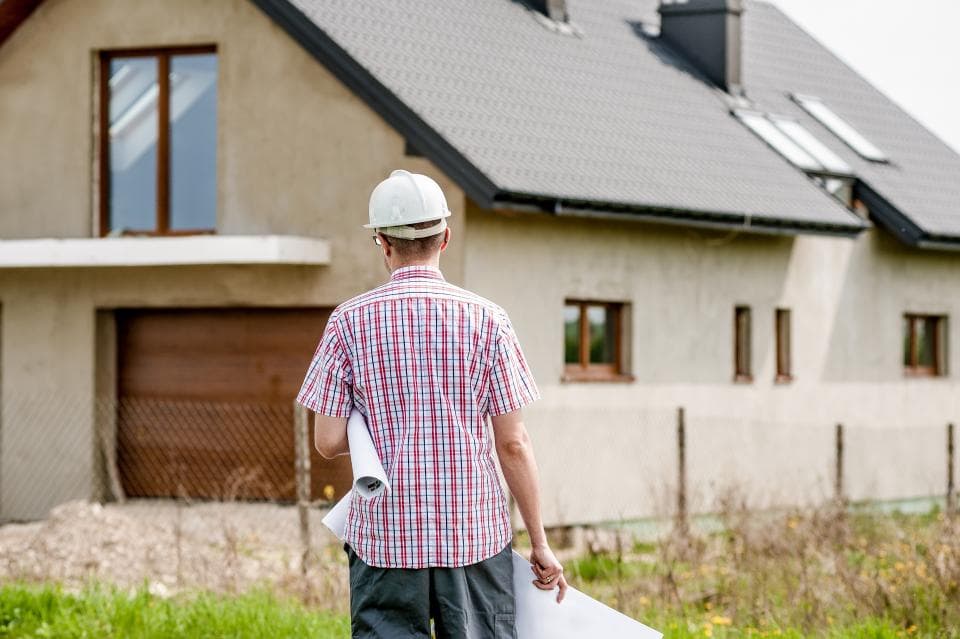 Bouwer met helm en tekeningen onder de arm voor een woning in aanbouw