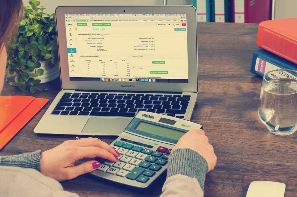 Iemand werkt met een rekenmachine naast een laptop met een spreadsheet